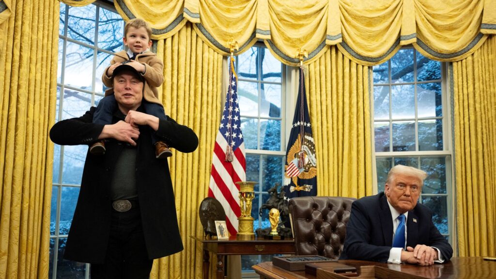 Elon Musk carries his son X Æ A-Xii on his shoulders while speaking as US President Donald Trump looks on in the Oval Office of the White House.