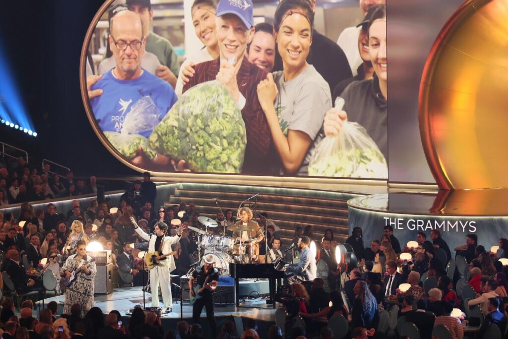 Dawes opens the 67th Grammys with "I Love L.A." below large image of people holding bags of supplies.