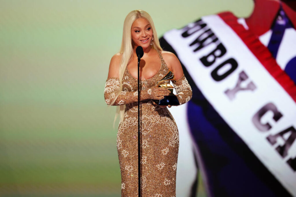 Beyoncé at the microphone, in front of a red, white and blue banner saying