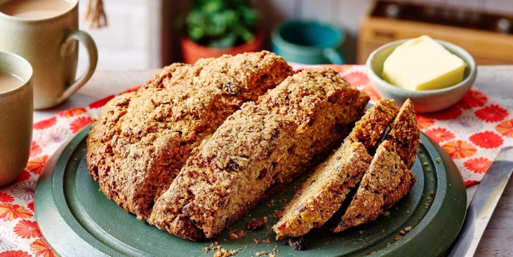 sliced soda bread on a wooden chopping board with a floral table cloth and house plant in the background