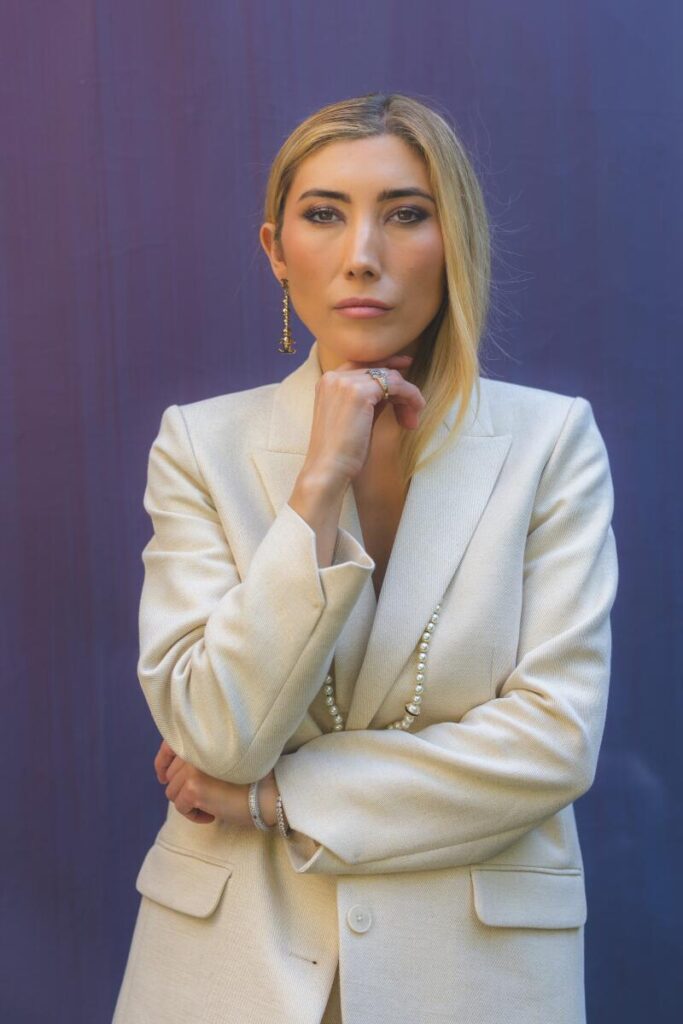 A woman in a white suit jacket holding her hand to her chin.